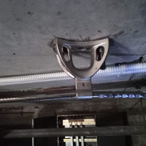 Imagen detallada de un sistema de anclaje de seguridad instalado en un techo de hormigón, con cables y conducciones eléctricas en segundo plano, representando los estándares de seguridad en la rehabilitación y refuerzo estructural de edificios.