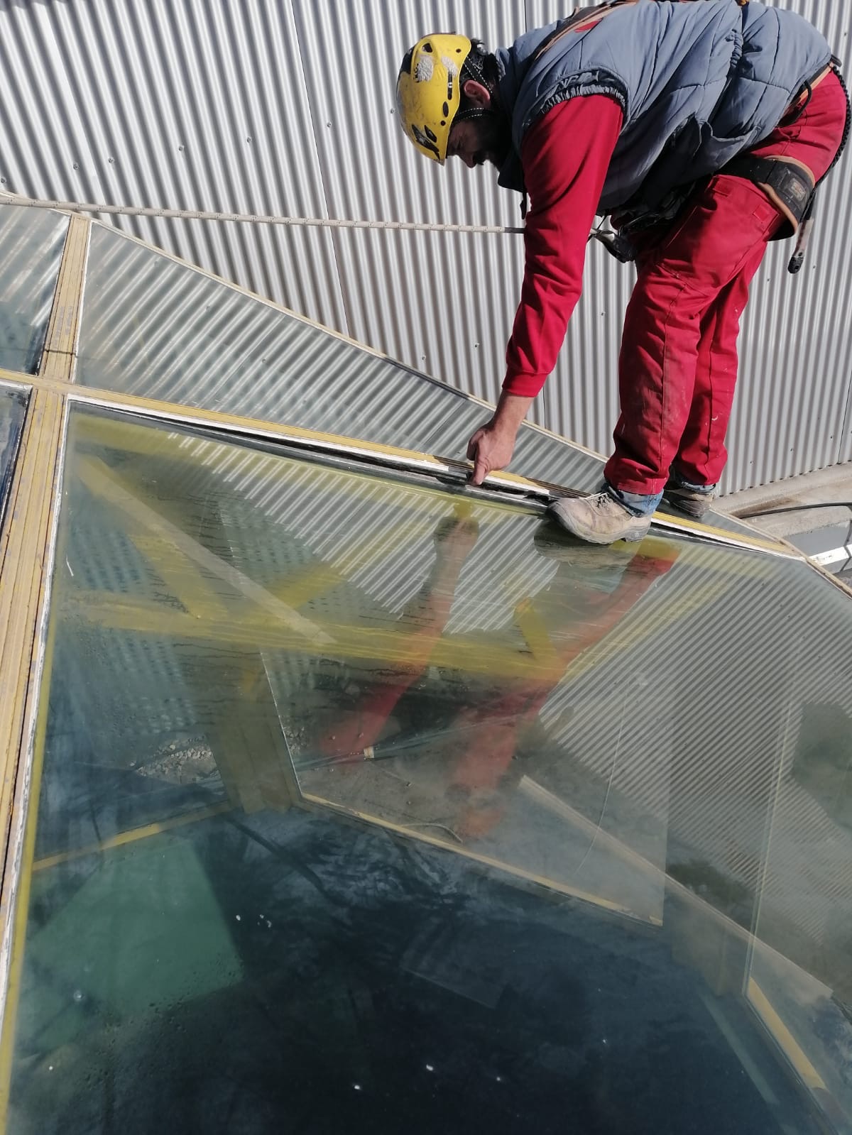 Un operario especializado en rehabilitación de edificios con casco amarillo y arnés de seguridad, trabajando cuidadosamente sobre una cúpula de cristal. La fotografía muestra el proceso meticuloso y la pericia necesaria para mantener y restaurar los elementos de vidrio en la arquitectura moderna.